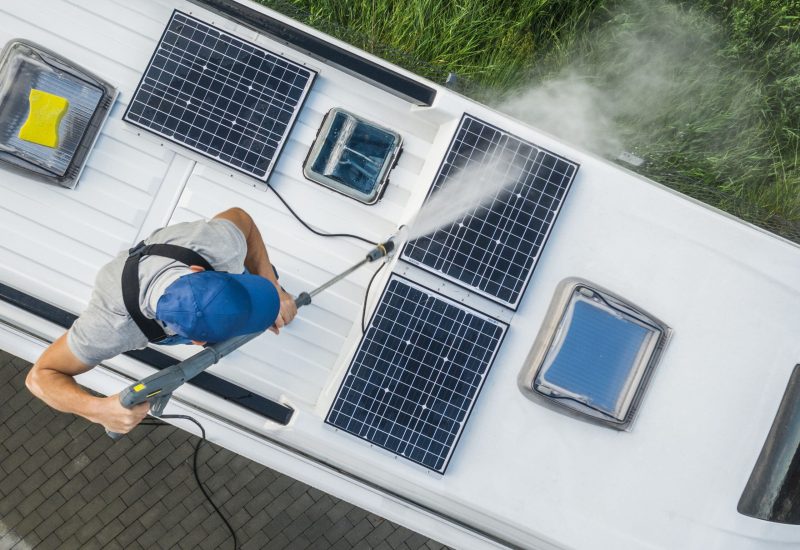 Caucasian Men Power Washing His Camper Van RV Roof and Solar Panels. Cleaning Modern Motorhome Using Pressure Washer.